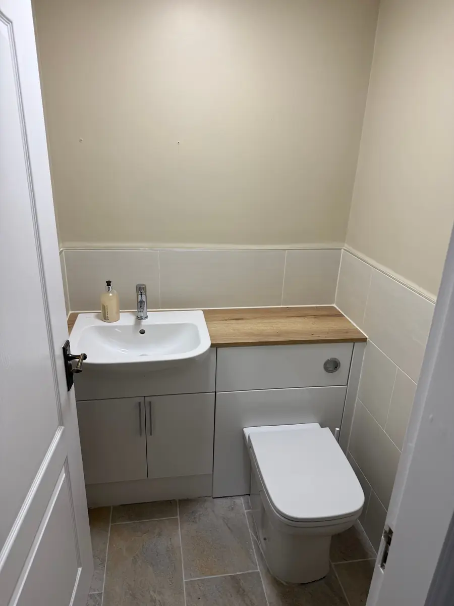 Refitted cloakroom with a grey vanity unit, oak-effect worktop, back-to-wall toilet and new tiling